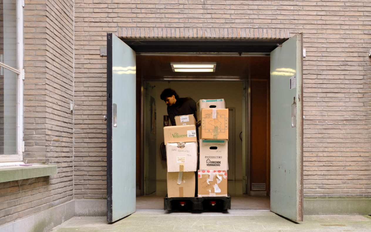 Een medewerker van het Letterenhuis transporteert een pallet met dozen vol archiefstukken naar binnen.