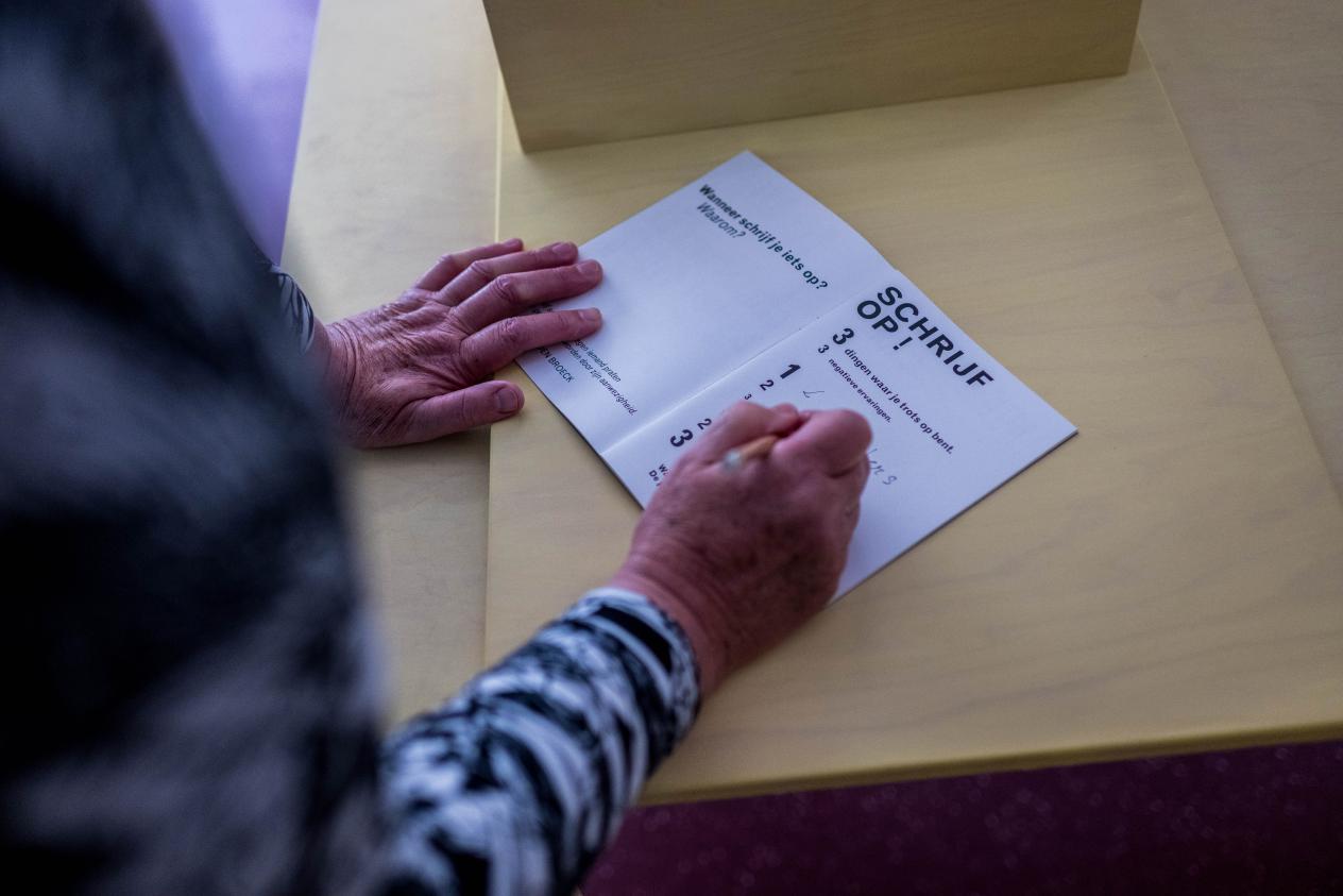 Een opdrachtboekje ligt opengeslagen op een tafel. De persoon die het boekje vasthoudt noteert op de rechterpagina.