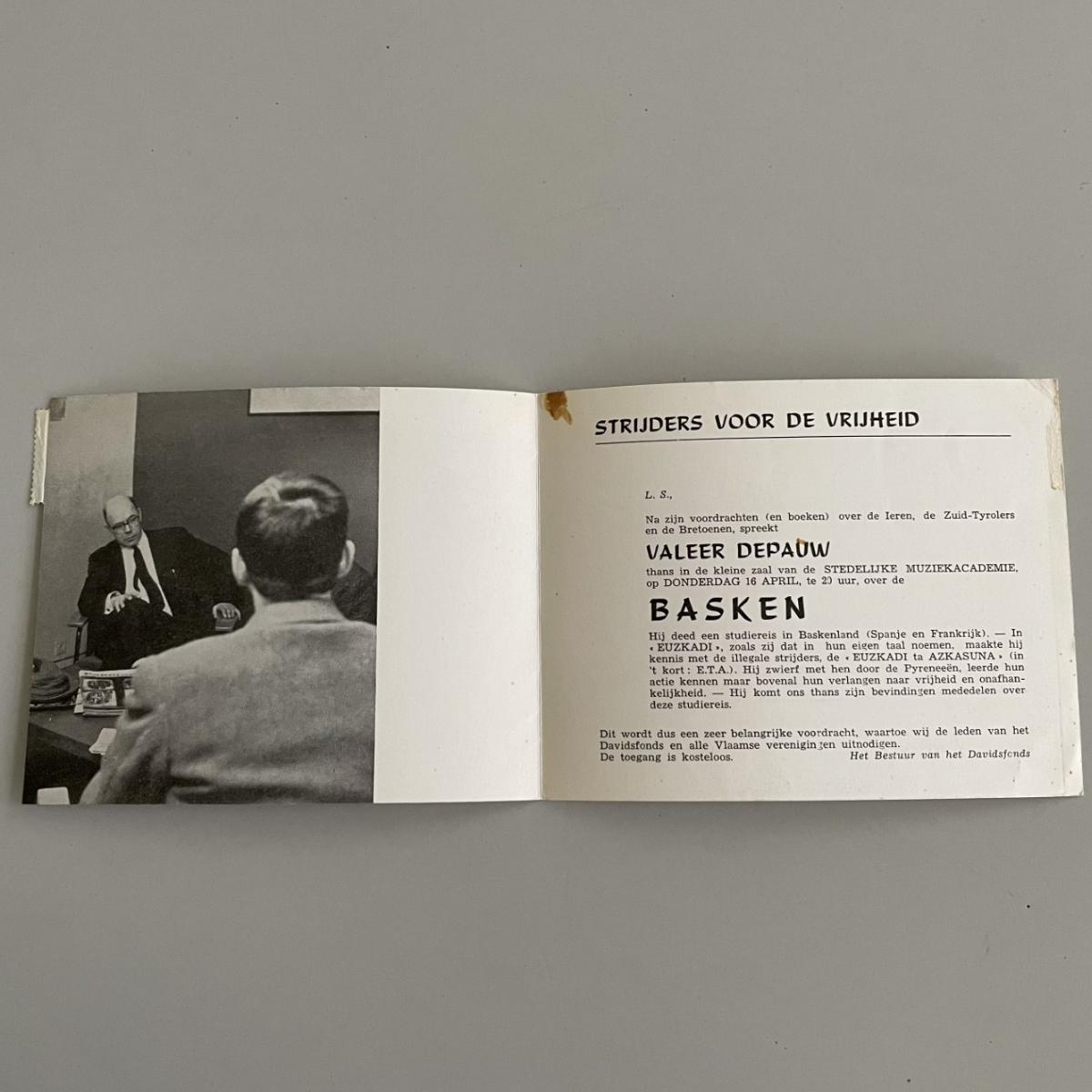 Opengevouwde uitnodigingskaart met aan de linkerkant een zwartwitfoto van twee mannen die een conversatie voeren. Aan de rechterkant staat de tekst van de uitnodiging voor de lezing over de Basken.