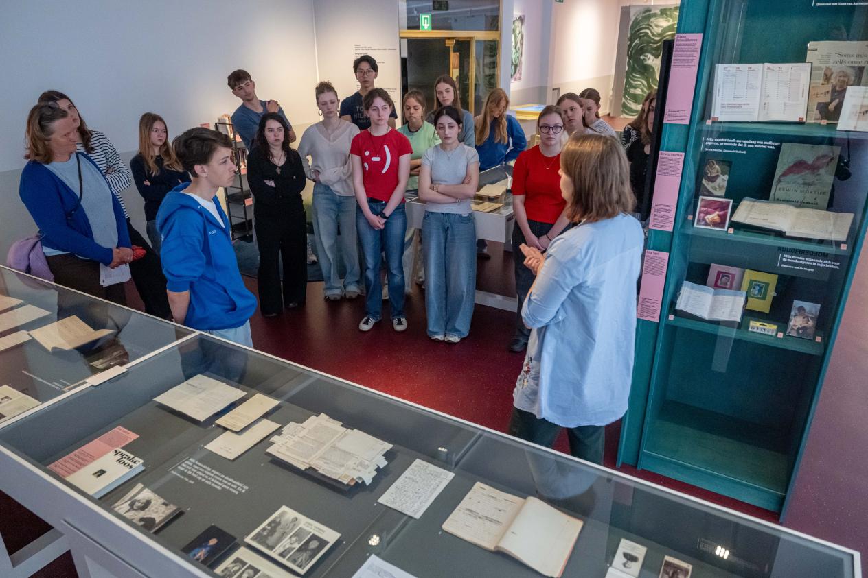 Een klas middelbare scholieren, 3de graad, staat in de thema-expo Moeders en luistert naar de uitleg van de workshopbegeleider over de expo en het onderwerp Moeders.