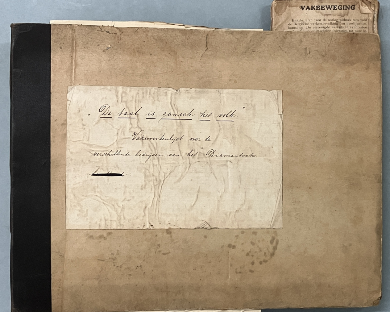 De voorkaft van de vakwoordenlijst voor ambachten uit de diamantverwerking. In sierlijk handschrift erop genoteerd de tekst: De taal is gansch het volk. Vakwoordenlijst over de verschillende bedrijven van het diamantvak.