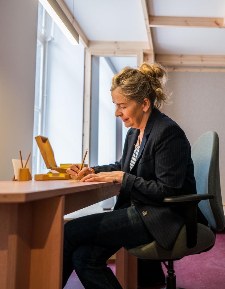 Ilse Ceulemans zit aan de schrijftafel in de schrijfkamer terwijl ze op een notitieblaadje schrijft