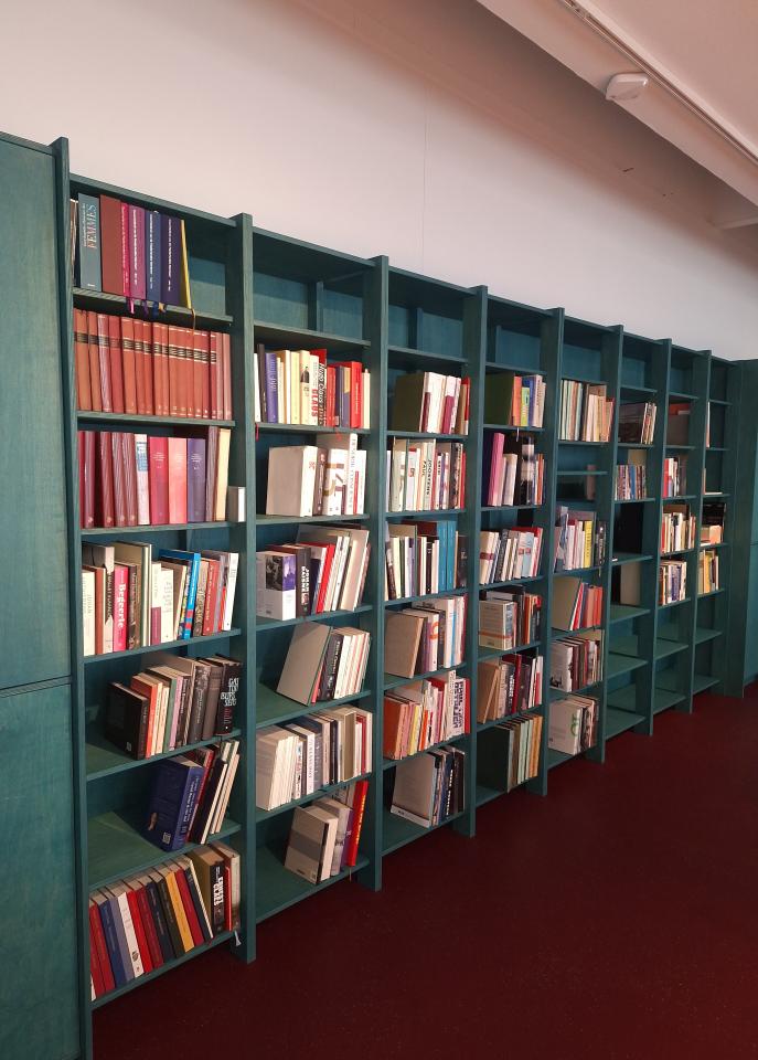 Foto van de groene boekenkasten in de leeszaal, gevuld met publicaties.