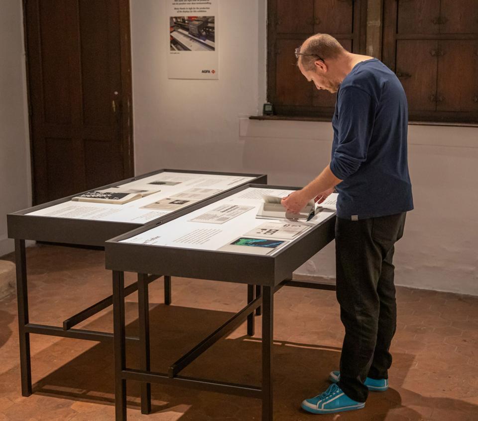 Een man bekijkt en bladert in boekontwerpen die op een toontafel liggen.