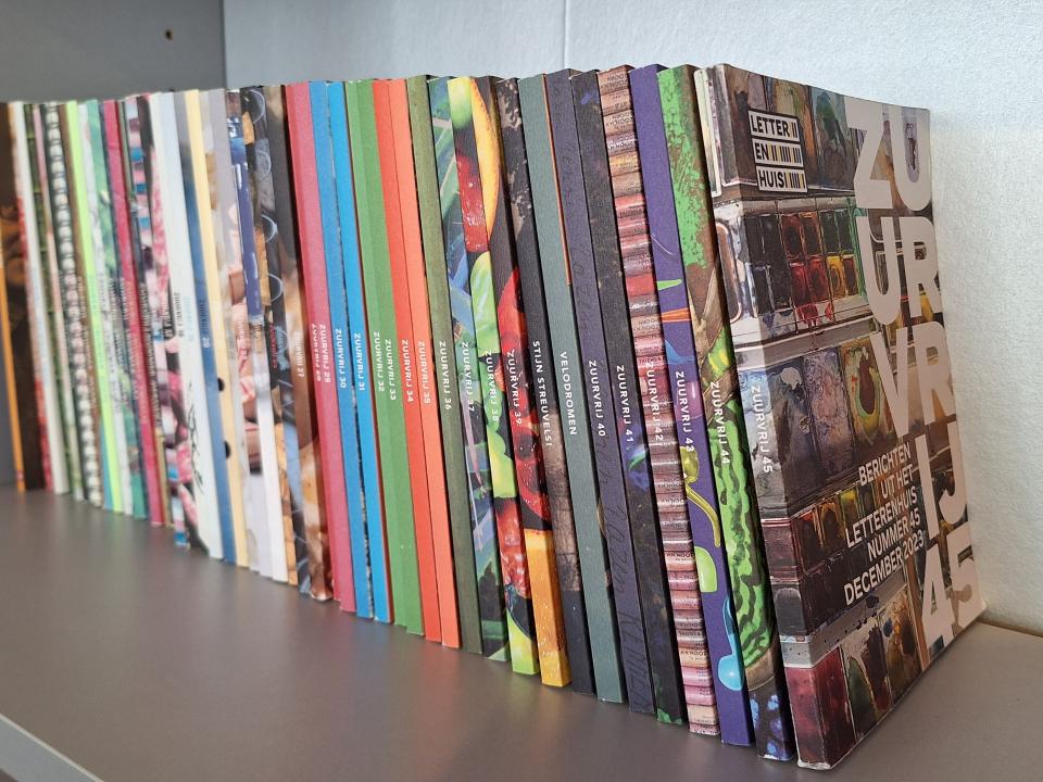 Een hele reeks kleurrijke nummers van Zuurvrij op een rijtje op een boekenschap in de leeszaal van het Letterenhuis