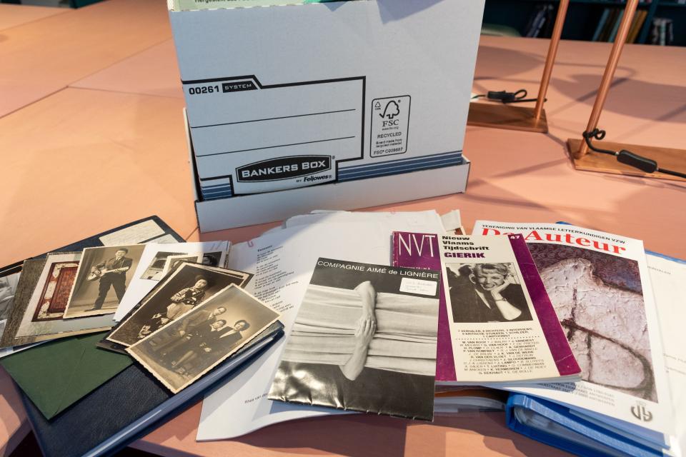 Een heleboel archiefstukken uit het archief van Rhea Van der Vloedt liggen uitgespreid op een tafel in de leeszaal van het Letterenhuis. Op de achtergrond zie je een verhuisdoos. Tussen de archiefstukken zitten zwartwitfoto's, tijdschriften, typoscripten van gedichten en nog veel meer.