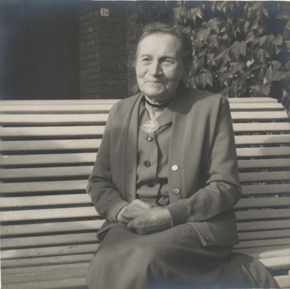 Alida Staelens, de echtgenote van schrijver Stijn Streuvels, zit op een tuinbank mat haar handen in elkaar.