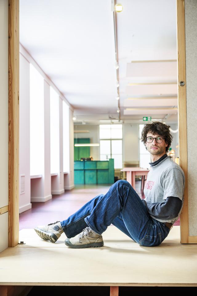 Portretfoto van Tomas Van Balen zitten in de deuropening van de schrijfkamer met de leeszaal op de achtergrond