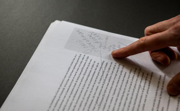 Een hand wijst een notitie bij een manuscript aan