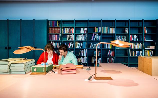 Twee dames in de leeszaal omringd door archiefmappen