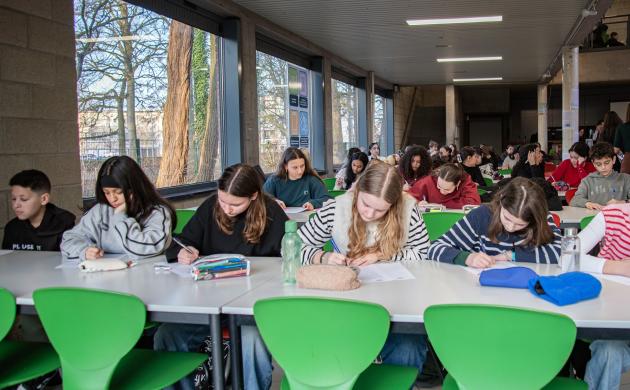 Kinderen van Pius 10 zitten schrijvend aan tafels in de cafetaria
