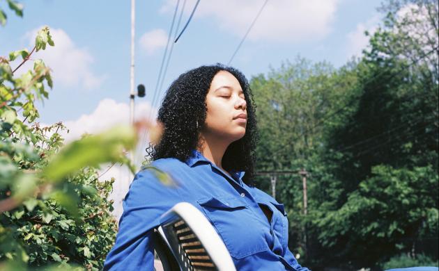 Portretfoto van Emma Hessels op een stoel met bomen en blauwe lucht op de achtergrond