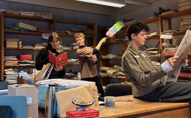 Je ziet de jongerenreporters, 1 meisje en 2 jongens, jonge twintigers, in een bureauruimte vol rommel en volle boekenkasten. Met een plumeau stoffen ze voorwerpen af, ze onderzoeken voorwerpen met een vergrootglas en doorbladeren oude kranten.