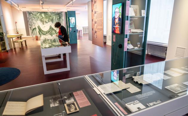 Een blik op de thema-expo Moeders: vitrinekasten met archiefmateriaal, boven één van de lage kasten staat een vrouw gebogen die de stukken bekijkt.