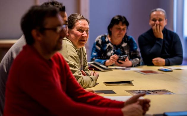Een groep volwassenen zit rond een tafel en luistert aandachtig naar de leerkracht