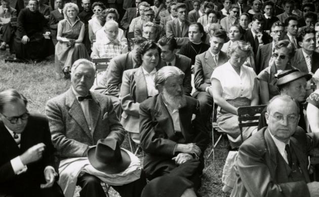 Zwartwitfoto van een hele groep deftig geklede mensen op houten klapstoelen in een tuin
