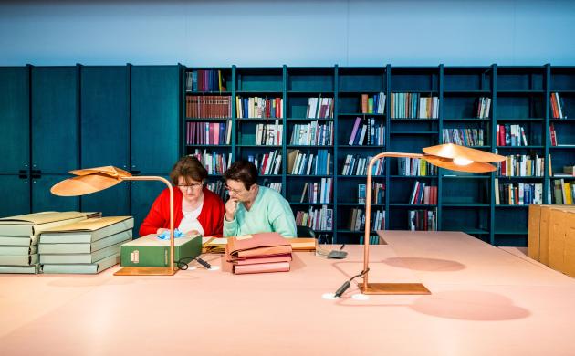 Twee dames in de leeszaal omringd door archiefmappen