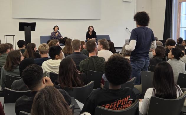 Een volle zaal scholieren luistert naar Hind Eljadid. Eén jongen staat recht om een vraag te stellen.