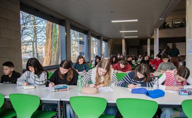 Kinderen van Pius 10 zitten schrijvend aan tafels in de cafetaria