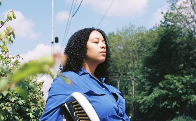 Portretfoto van Emma Hessels op een stoel met bomen en blauwe lucht op de achtergrond