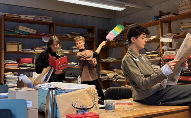 Je ziet de jongerenreporters, 1 meisje en 2 jongens, jonge twintigers, in een bureauruimte vol rommel en volle boekenkasten. Met een plumeau stoffen ze voorwerpen af, ze onderzoeken voorwerpen met een vergrootglas en doorbladeren oude kranten.