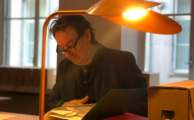 Vitalski aan een tafel in de leeszaal van het Letterenhuis terwijl hij het archief van Rhea Van der Vloedt doorbladert