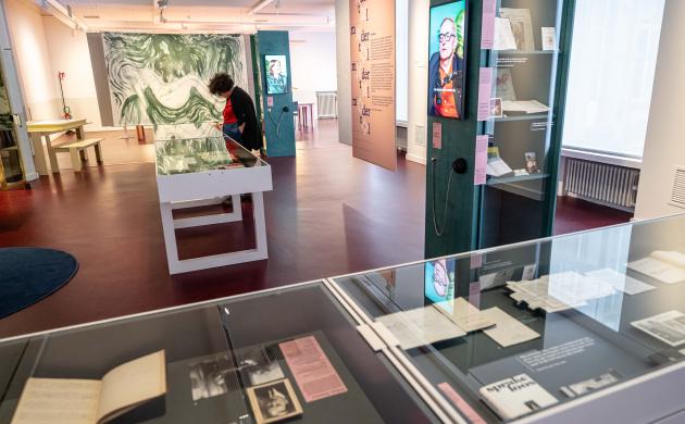 Een blik op de thema-expo Moeders: vitrinekasten met archiefmateriaal, boven één van de lage kasten staat een vrouw gebogen die de stukken bekijkt.