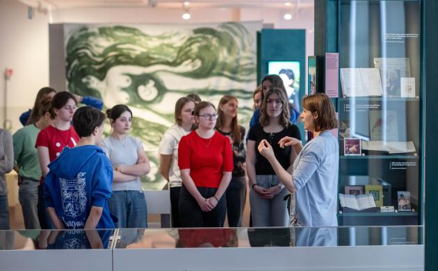 Een gids vertelt aan een groep leerlingen meer over de expo in de publieksruimte van het Letterenhuis.