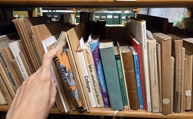 Boeken in een boekenrek. Een hand haalt een boek uit het rek.